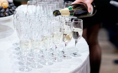 waiter pours champagne into arranged glasses on white table