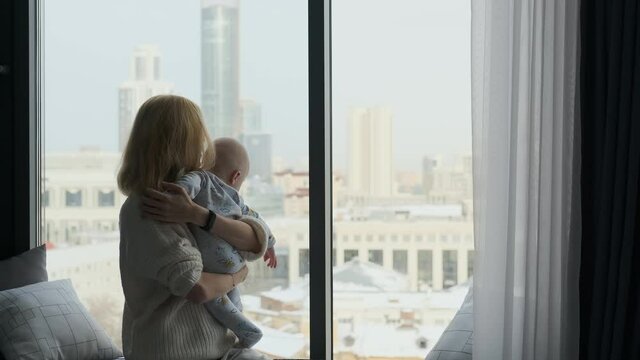 Mom With Son In Her Arms Look Out The Window At The City