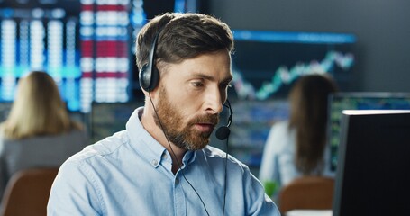 Portrait of man trader or broker working at stock exchange office using headset and computer on background of his business team. Investment Entrepreneur Trading Concept.