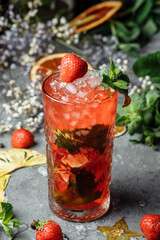 Strawberry Mojito. Cold summer mojito cocktail with strawberries, mint, lemon and ice in a glass on a table. on a dark background