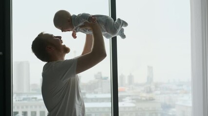 happy man picks up his child son while standing by the window