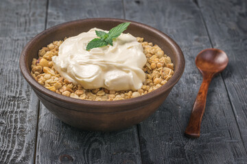 Granola with yogurt in a clay bowl on a rustic table.