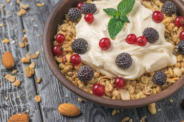 Granola with yogurt, raspberries and currants in a clay bowl on a rustic table.