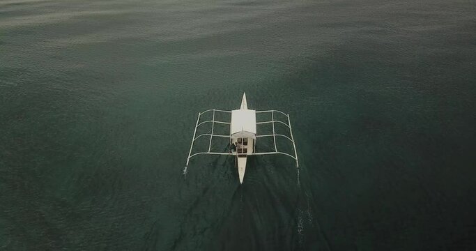 A small white tourist boat or banca sailing through the sea off Bohol during overcast weather. Boat exits scene at end.