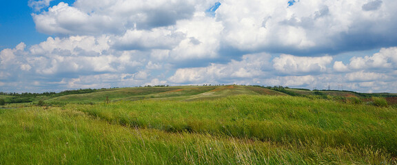 Summer natural landscape, meadow, field, hills. Beautiful blue sky with clouds.