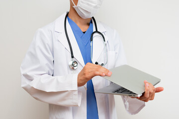 パソコンを抱えて仕事をする白衣を着た男性医師