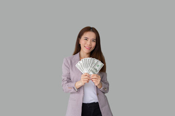 Portrait of smiling beautiful Asian woman holding lot of money banknotes and smiling isolated over grey color background