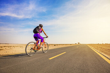 Fototapeta premium Young woman riding a bicycle in a desert in Dubai, full length shot