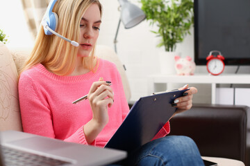 young beautiful blond woman sit on the sofa in livingroom hold binder in arms work with laptop listen to music sunny morning concept