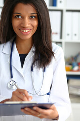 Beautiful smiling black female doctor hold clipboard pad and fill something with silver pen. Physical illness prevention prescribe remedy ward round therapeutist assistance healthy lifestyle concept