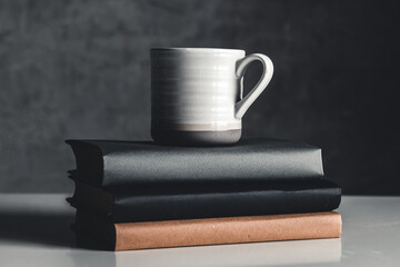 A cup of coffee on stack of books on grey background