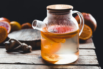 Citrus tea in a transparent teapot and a glass, healthy drink on a wooden background.