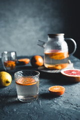 Citrus tea in a transparent teapot on a dark concrete background. Healthy drink, vegan, eco product.