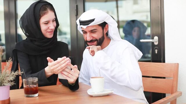 Arab couple watching photos on phone in a cafe