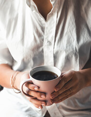 Woman in a white t-shirt holds morning coffee in a pink ceramic cup. Manicure. Front view