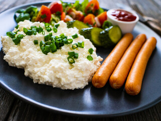 Breakfast - cottage cheese, boiled sausages and vegetables served on wooden table
