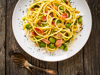 Spaghetti with broad bean, bacon and parmesan on wooden table
