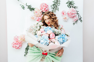 Beautiful girl with beautiful makeup on her face and hairstyle with a large luxurious bouquet of flowers, advertising for cosmetologists and florists with decorators