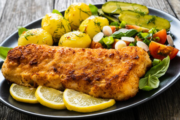 Fish dish - fried breaded cod fillet with vegetables on wooden table
