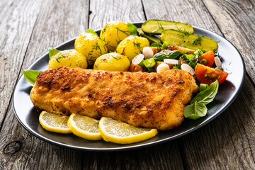 Fish dish - fried breaded cod fillet with vegetables on wooden table
