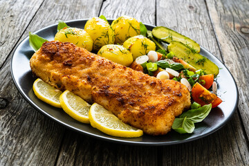 Fish dish - fried breaded cod fillet with vegetables on wooden table
