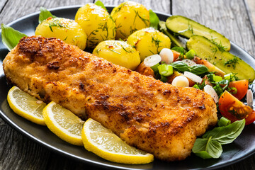 Fish dish - fried breaded cod fillet with vegetables on wooden table
