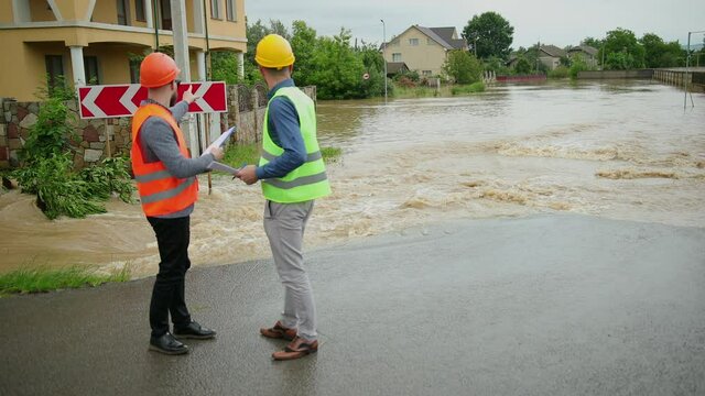 Two male engineers solve flood problem. Devastation wrought after massive disasters. Flooded outskirts of city. Traffic along overflowing with water street. Floods hit town. Heavy rain. Flooding.
