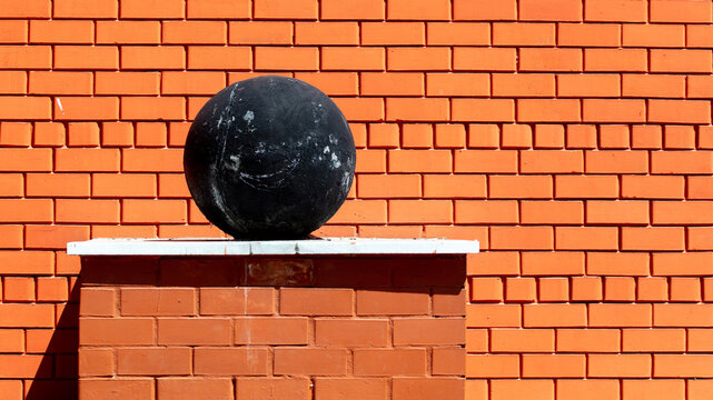 A large metal ball near a red brick wall. © schankz