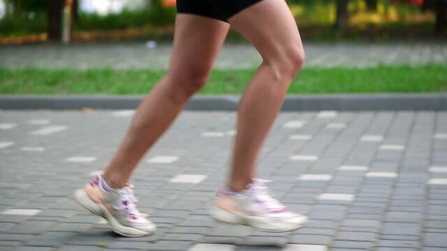 Female athlete's feet running at the park. Fitness woman jogging outdoors. Exercising on park pavement. Healthy, fitness, wellness lifestyle. Sport, cardio, workout concept. Side view. Slow motion