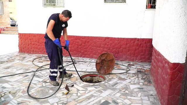 Worker cleans the drains hatch and removes dirt and debris from the sewer. Plumber cleans the sewer