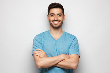 Young handsome man wearing blue tshirt, standing with crossed arms, isolated on gray background