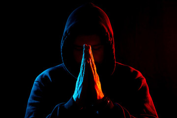 a man in dark clothes in a hood on a dark background folded his hands for prayer