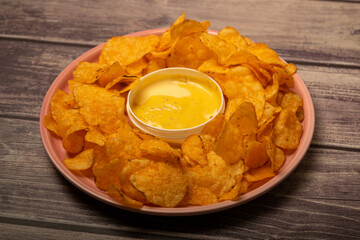 Potato chips on a round platter and a saucepan with cheese sauce. Close up.