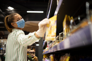 Grocery shopping during COVID-19 pandemic. Female person with mask and gloves buying food in supermarket.