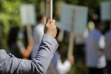 Shallow depth of field (selective focus) image with the hand of a man holding a wooden placard during a political rally.