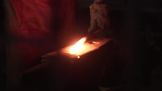 a gloved man is forging hot iron with a hammer on an anvil close up