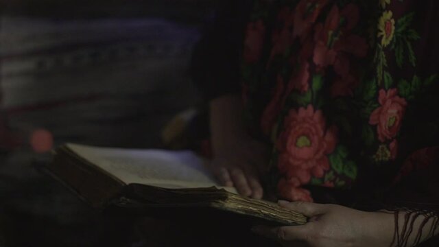 a grandmother in a Russian shawl reads a fairy tale from an old book by the light of a splinter in a hut
