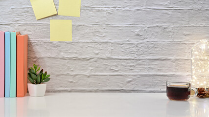 Cropped shot view of workspace with coffee cup, book and light bulb on white brick wall. Front view.