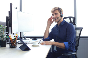 Happy young male customer support executive working in office. - obrazy, fototapety, plakaty