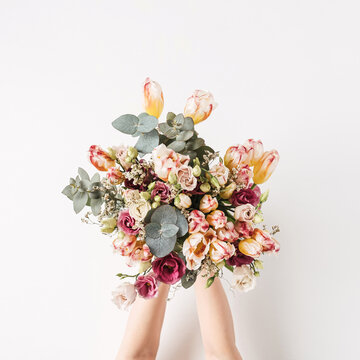 Female hand holding tulip, eucalyptus flowers bouquet against white wall. Holiday celebration festive floral concept