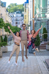 Guy and two girls bouncing up together on the street.