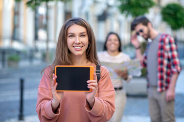 Smiling girl showing tablet screen on the street.