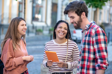 Cheerful three friends with a tablet on the street