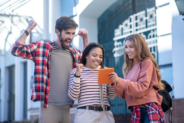 Two girls with tablet and guy rejoicing in the street