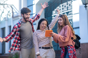 Girl with tablet and guy and girl raising hands near