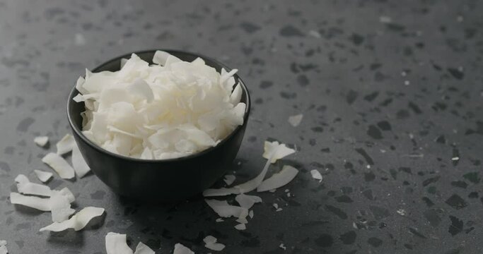 Handheld slow motion of coconut chips in black bowl on terrazzo surface