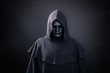 Scary figure with mask in hooded cloak in the dark