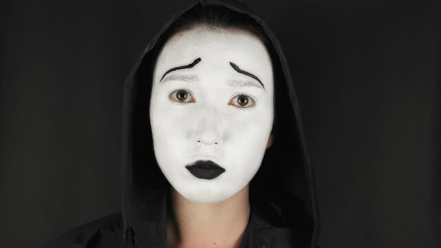 Brunette woman with white theatrical mask and make-up on her face. Sad girl takes off the theatrical mask from her face and looks at the camera. Hide emotions. 