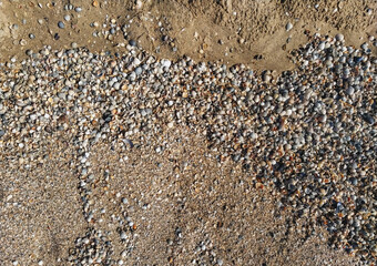 The texture of small, different-sized multi-colored sea shells mixed with gray and yellow sand. Photograph, top view.