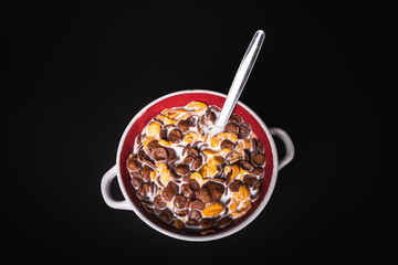 round bowl with colorful cornflakes and milk and a spoon isolated on black